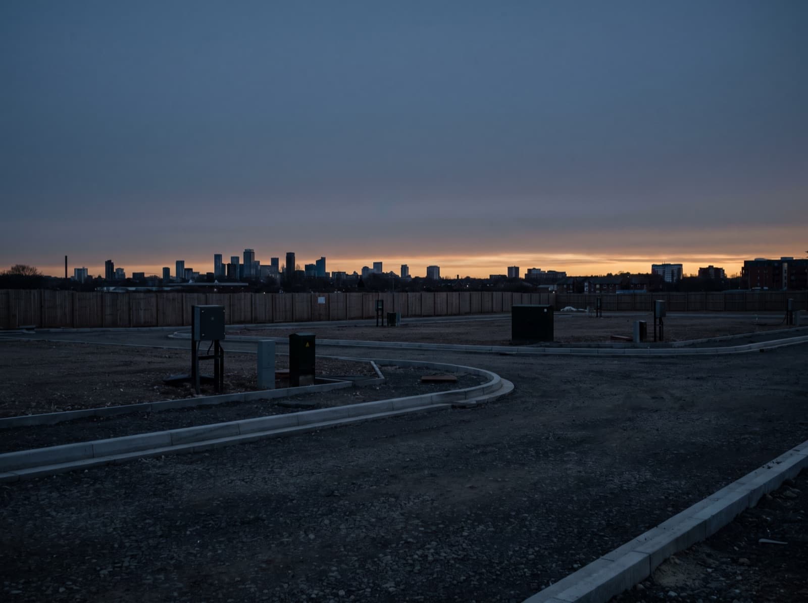 Cleared, serviced development site at dusk with a city skyline on the horizon