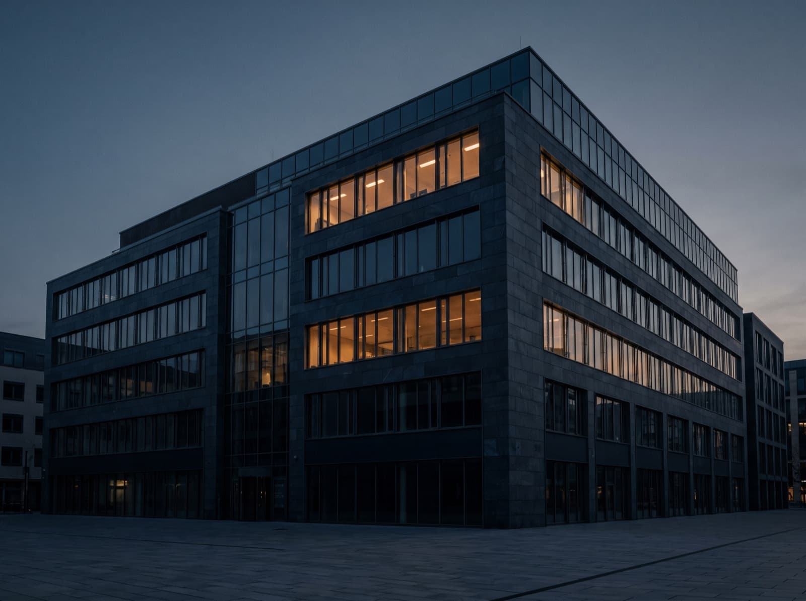 Mid-rise glass and stone office building at dusk with lit floors