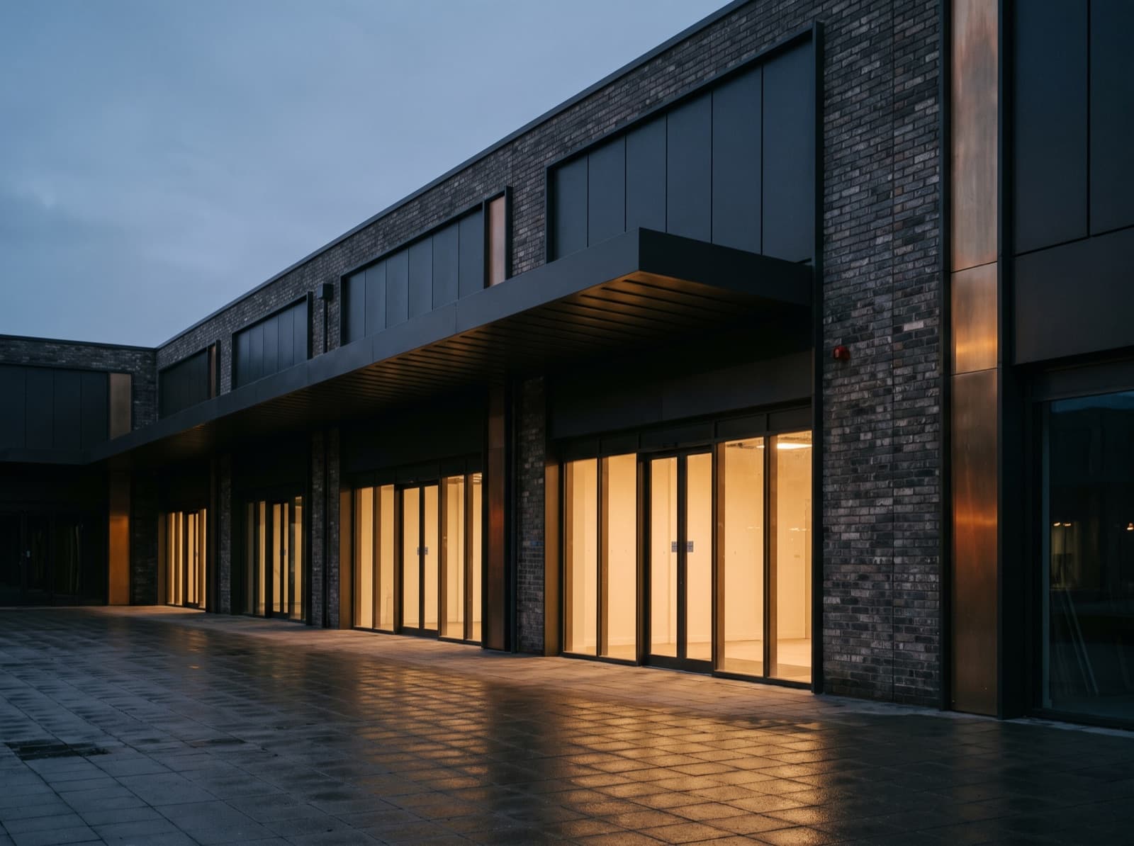 Single-storey retail parade at dusk with glazed shopfronts lit from within